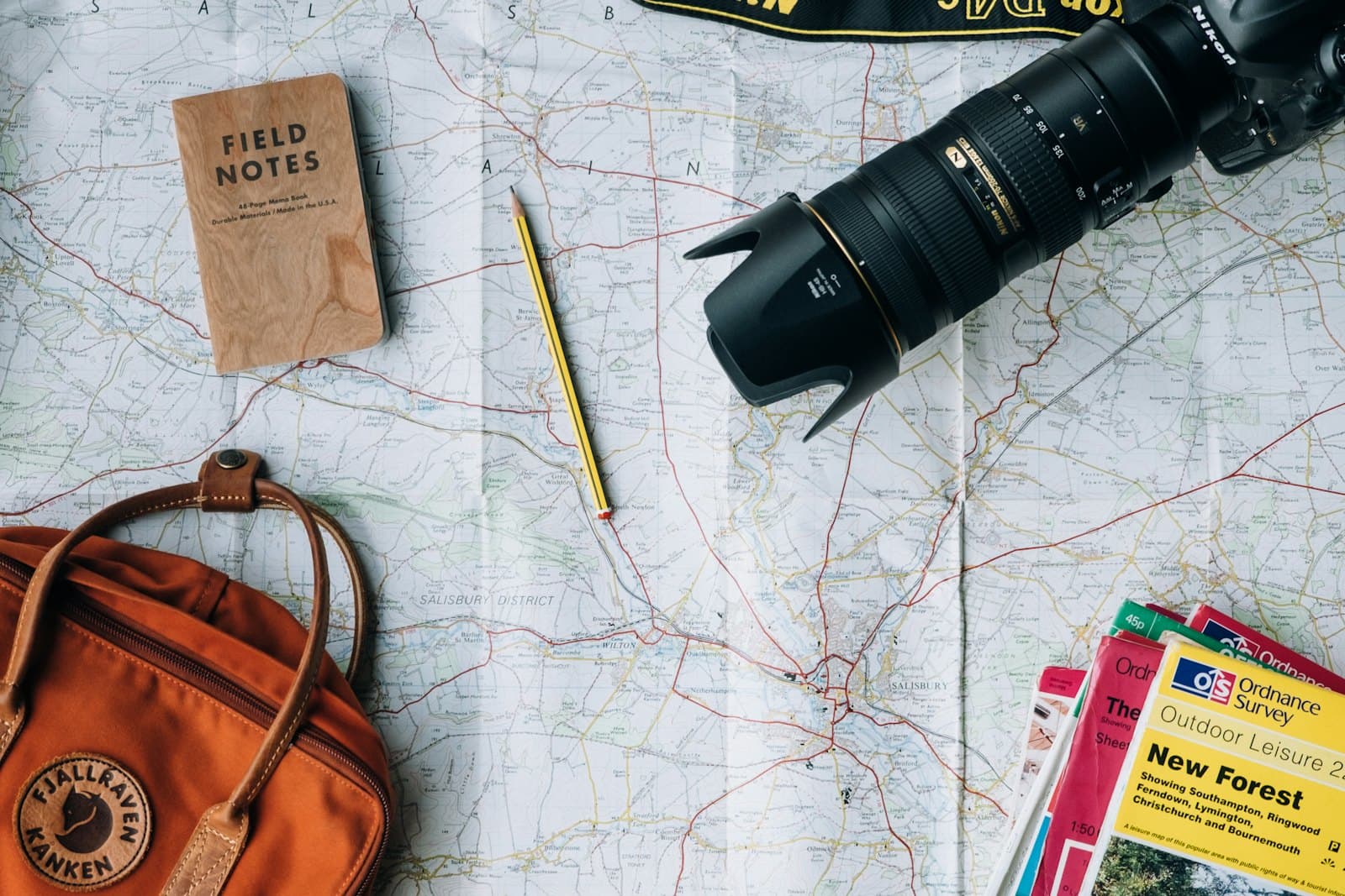 A notebook, a map and a camera on a wooden table, ready for planning a trip