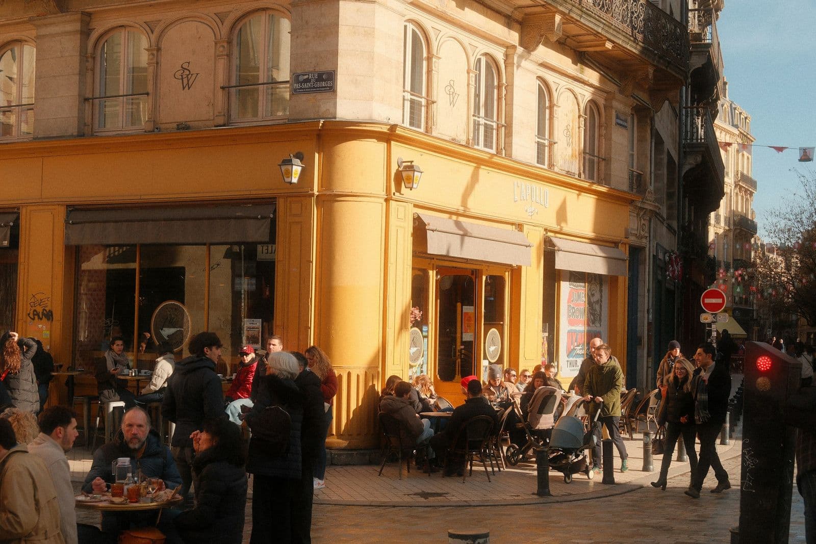 A street-corner café terrace with people sitting in late-afternoon sun