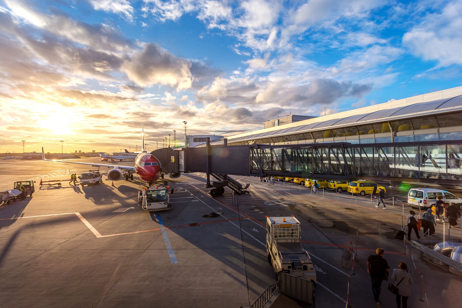 A plane at an airport gate at dusk, with travellers walking down to board