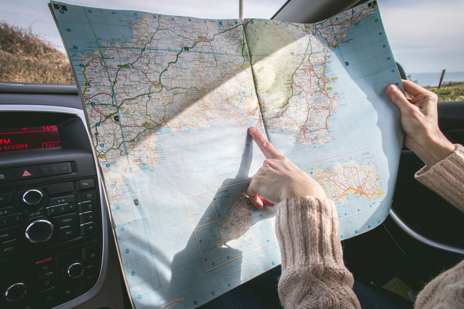 Hands pointing at a folded road map inside a car