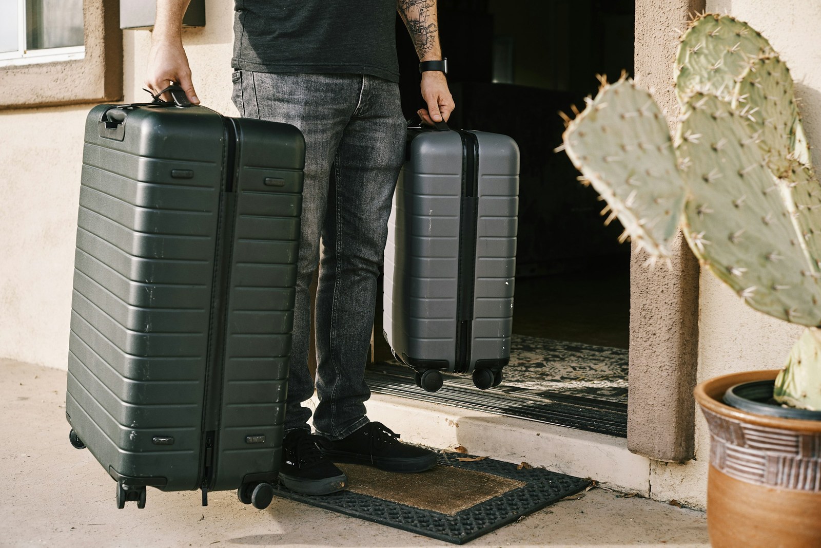 Someone at the front door, holding two suitcases, about to leave