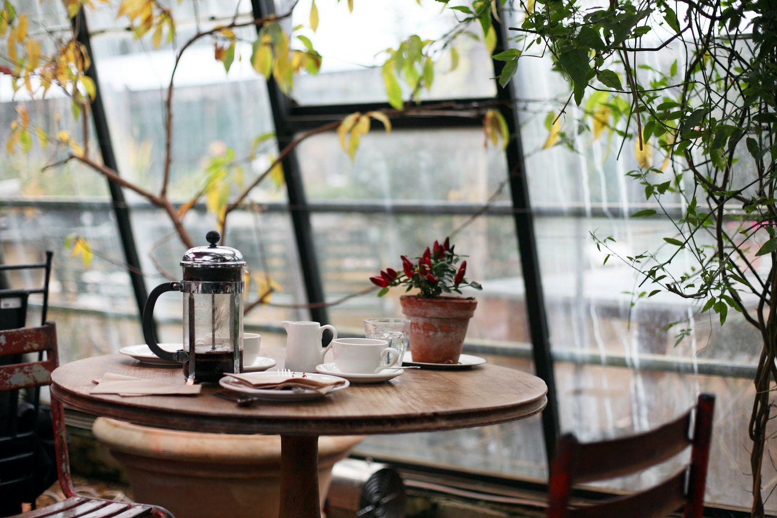 An empty café table by a window, with a coffee press and two chairs