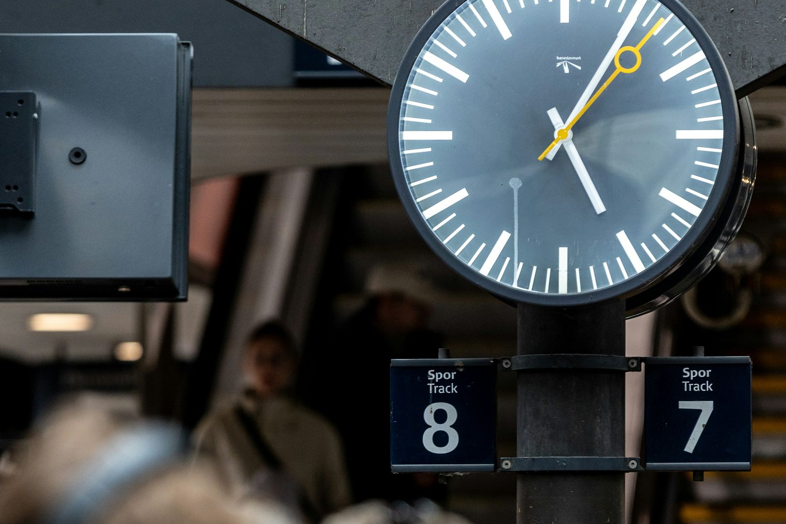 A station clock and platform numbers above a blurred crowd of travellers